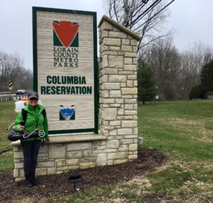 Owner of Mosquito Joe of Akron, Lori Wolff, with backpack spray in front of Lorain County Metro Parks Columbia Reservation sign.